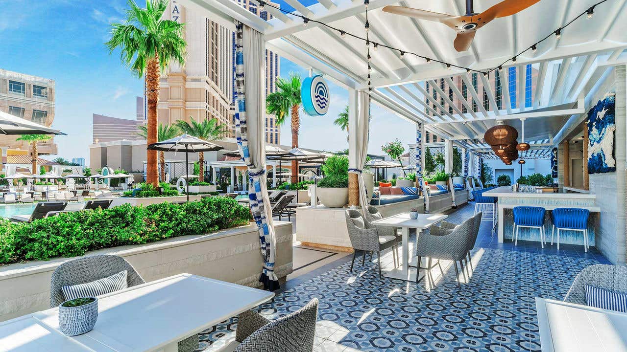 Outdoor patio dining area with tables and chairs next to a pool with lounge chairs and umbrellas.