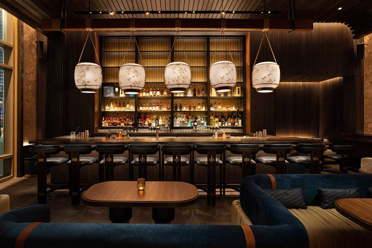 Elegant bar with modern lighting, fully stocked shelves, high stools at the counter, and cozy seating areas in the foreground.