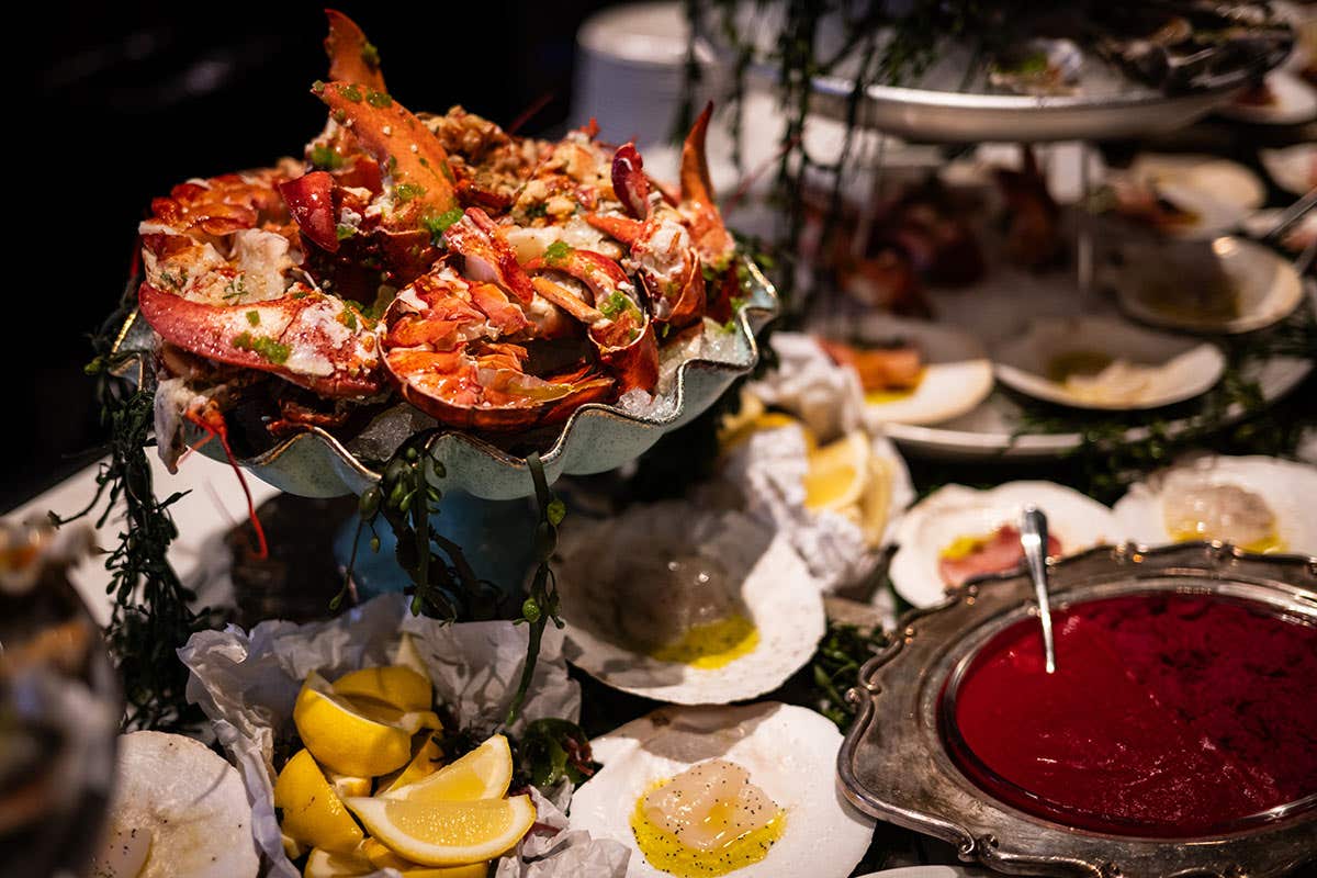 Seafood display featuring lobster, oysters, lemon wedges, and sauces on ice