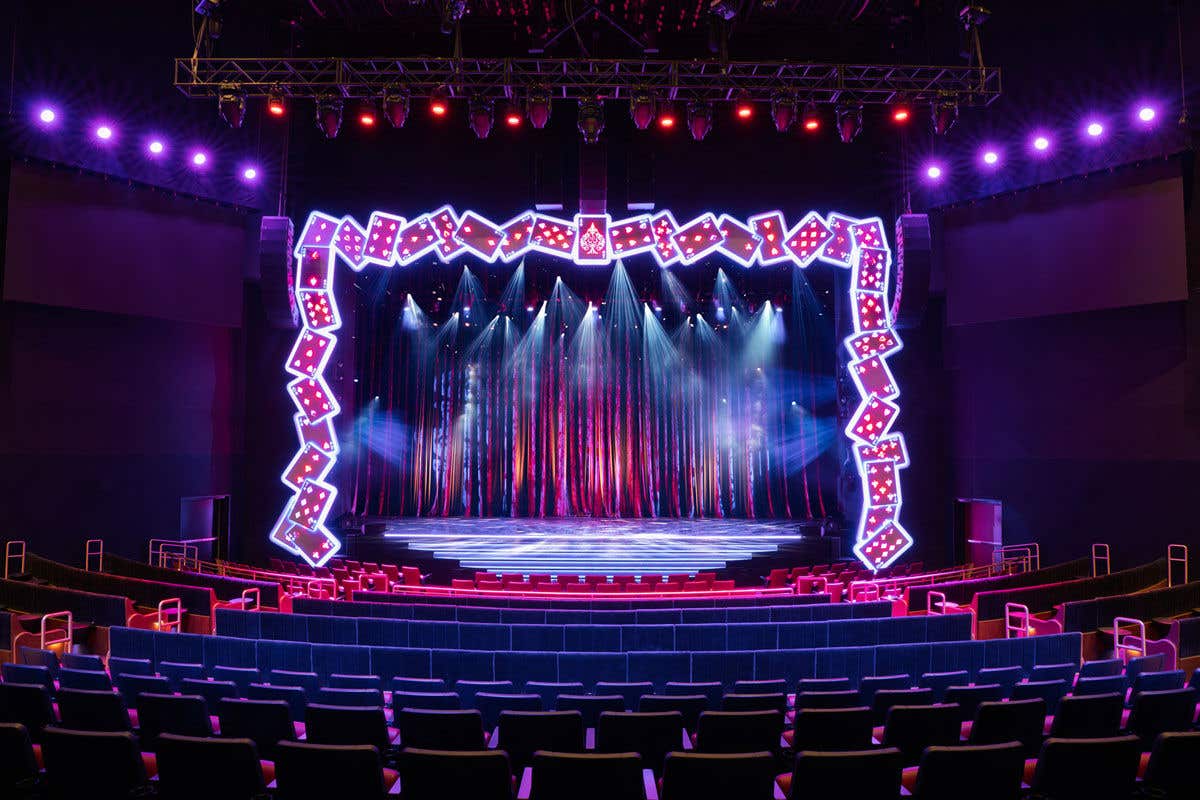 A colorful, illuminated stage with spotlights and bright lights, surrounded by rows of theater seats.