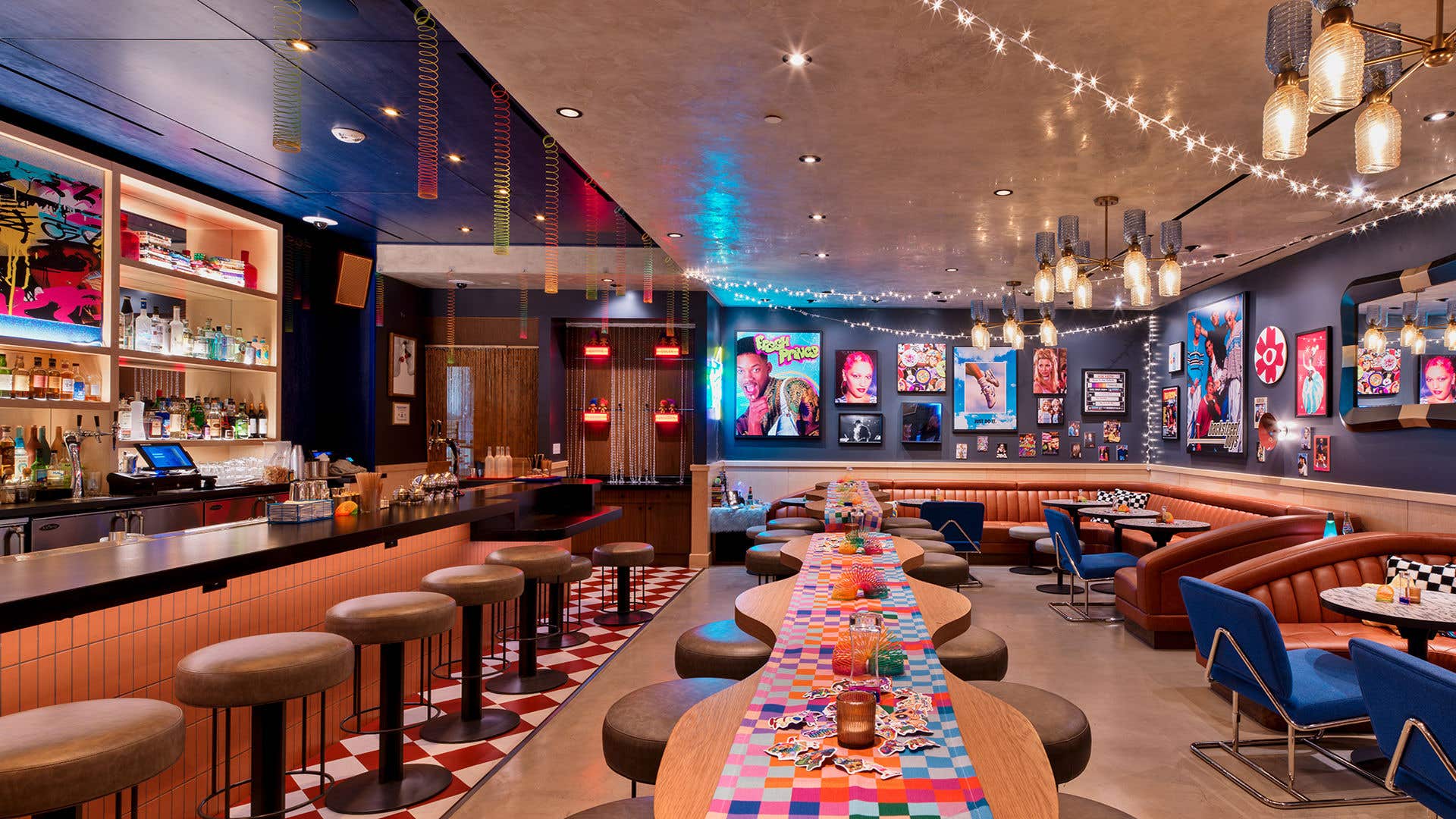 A bar with stool on the left, slinkies hanging down and neon art all around. High tops feature brightly colored runners, while the walls are filled with ‘90s memorability and string lights.