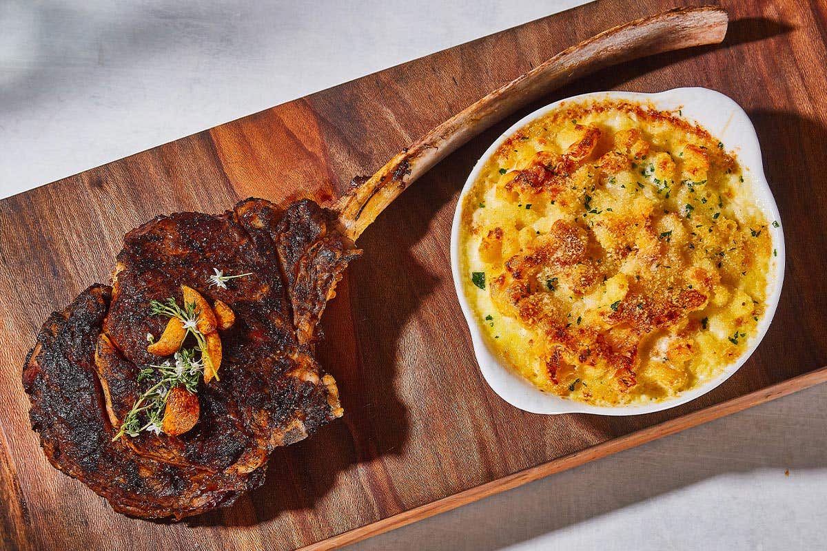 Tomahawk steak and mac and cheese on a wood plate. 