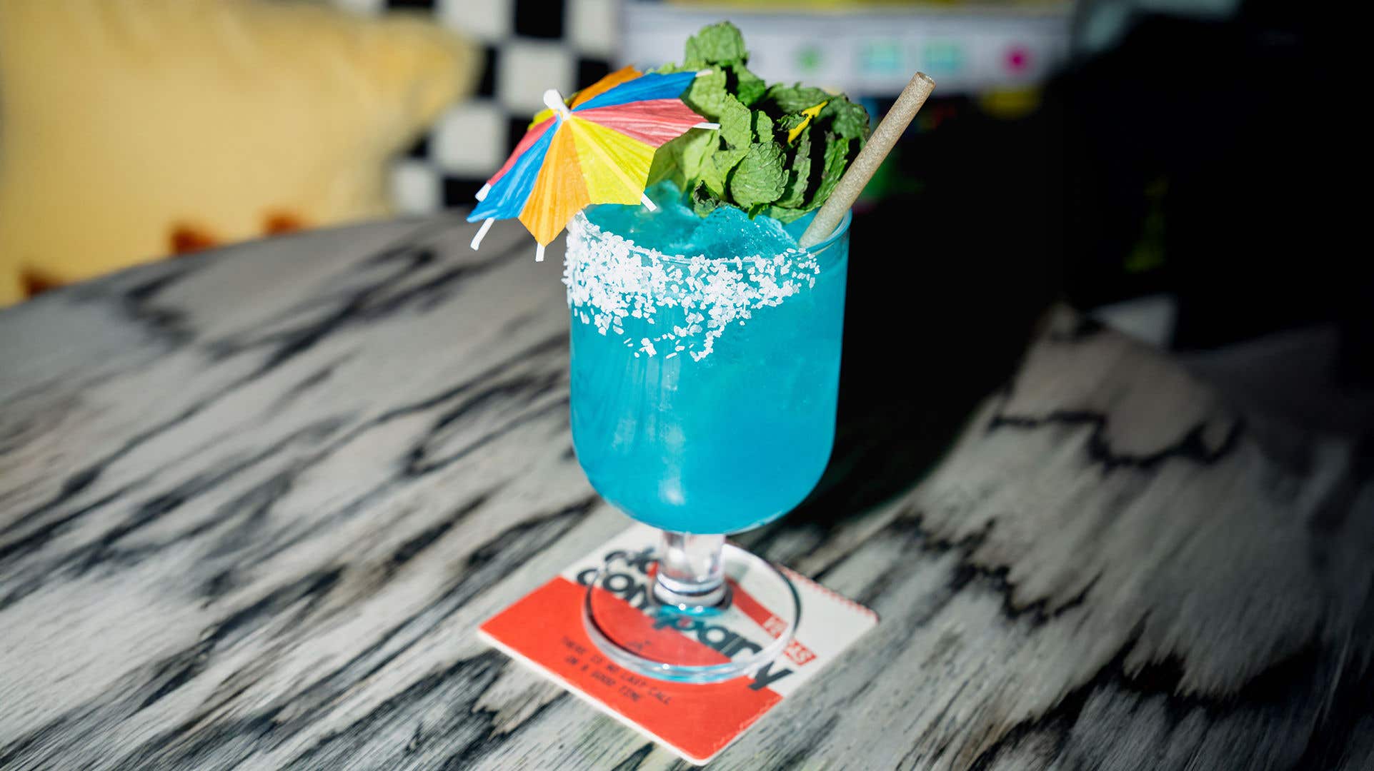 A bright blue drink garnished with an umbrella, mint and white coconut along the rim.