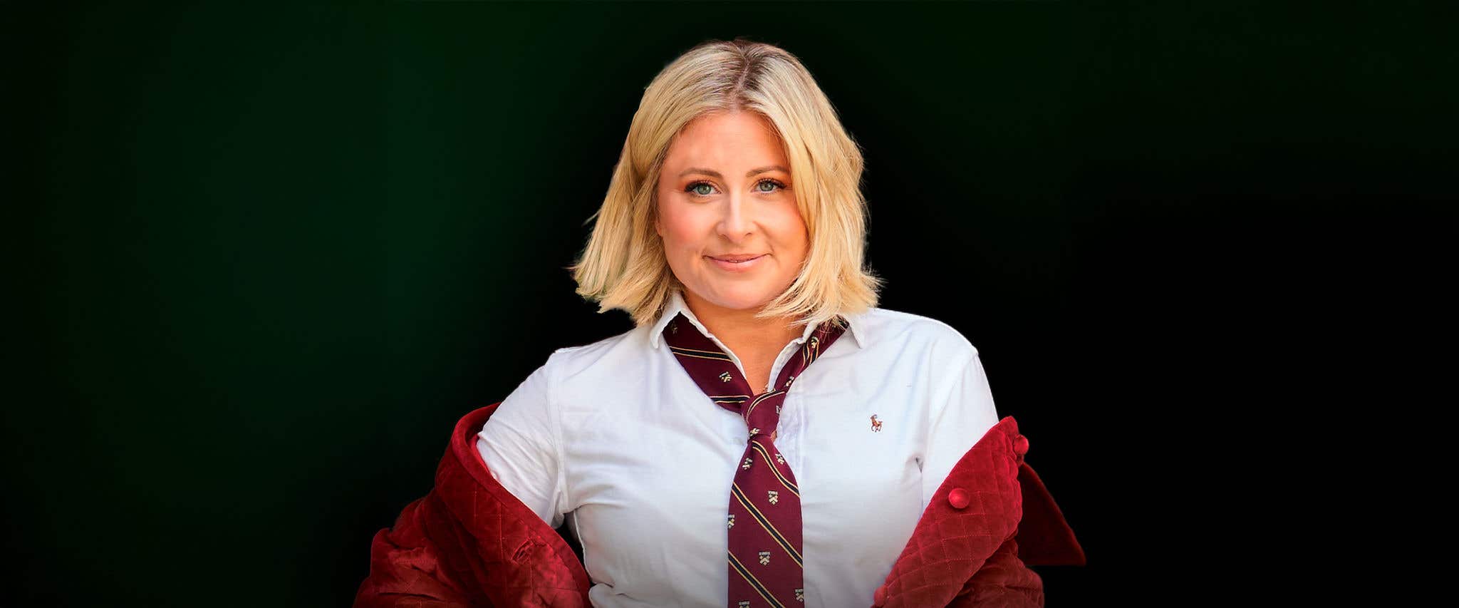 Becky Robinson wearing a white button-down shirt, a striped tie, and a red jacket draped over the shoulders, posed against a dark background.