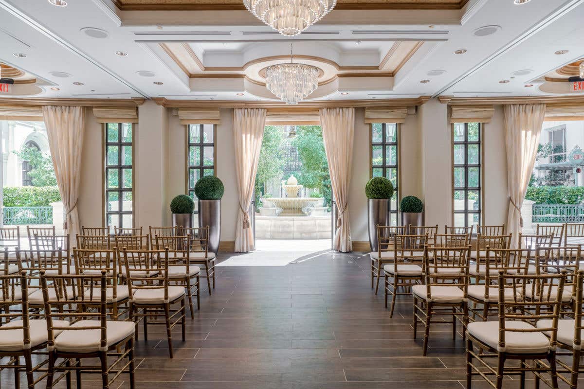 An event venue space with gold chairs set up around an aisle leading to open doors letting out onto a patio with a water fountain.