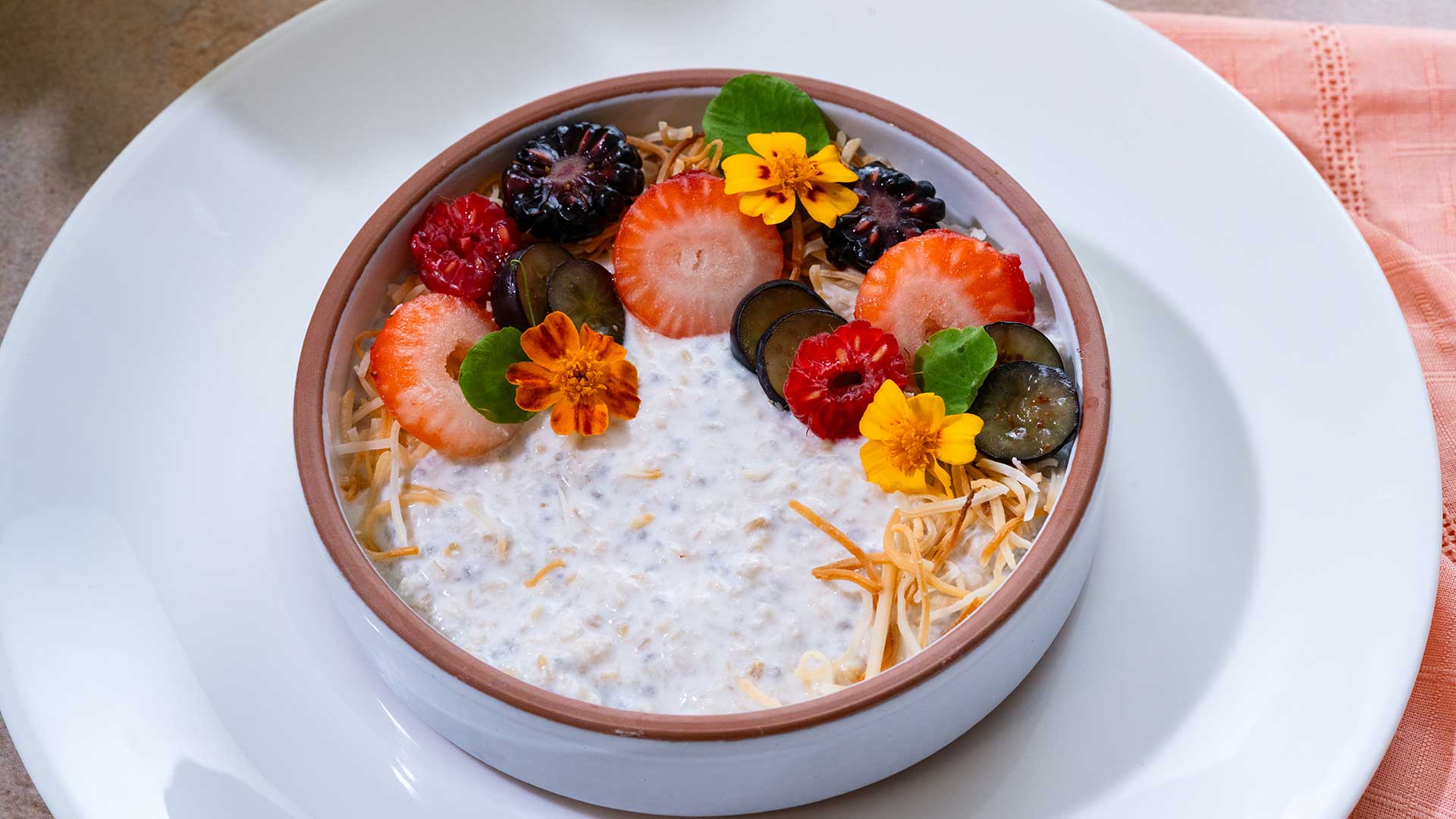Bowl of creamy oatmeal garnished with strawberries, berries, grapes, shredded coconut, and edible flowers.