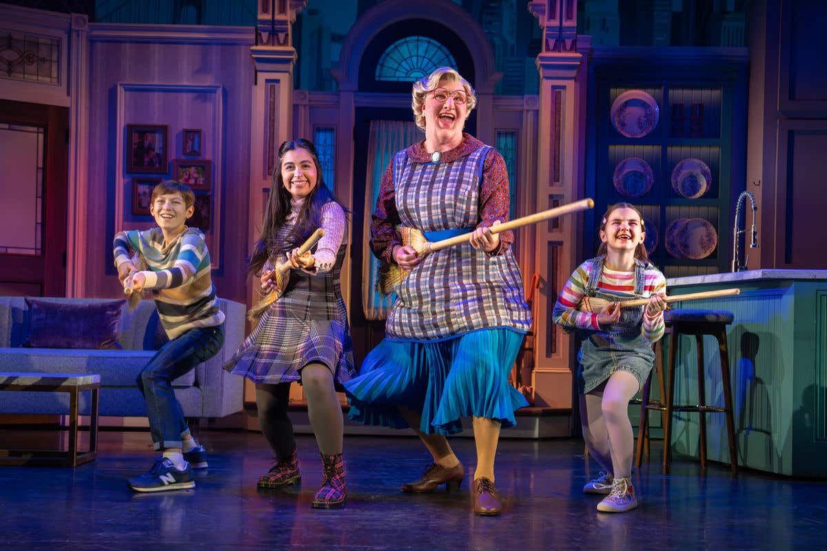 Mrs. Doubtfire holding a broom with the kids on each side of her. 