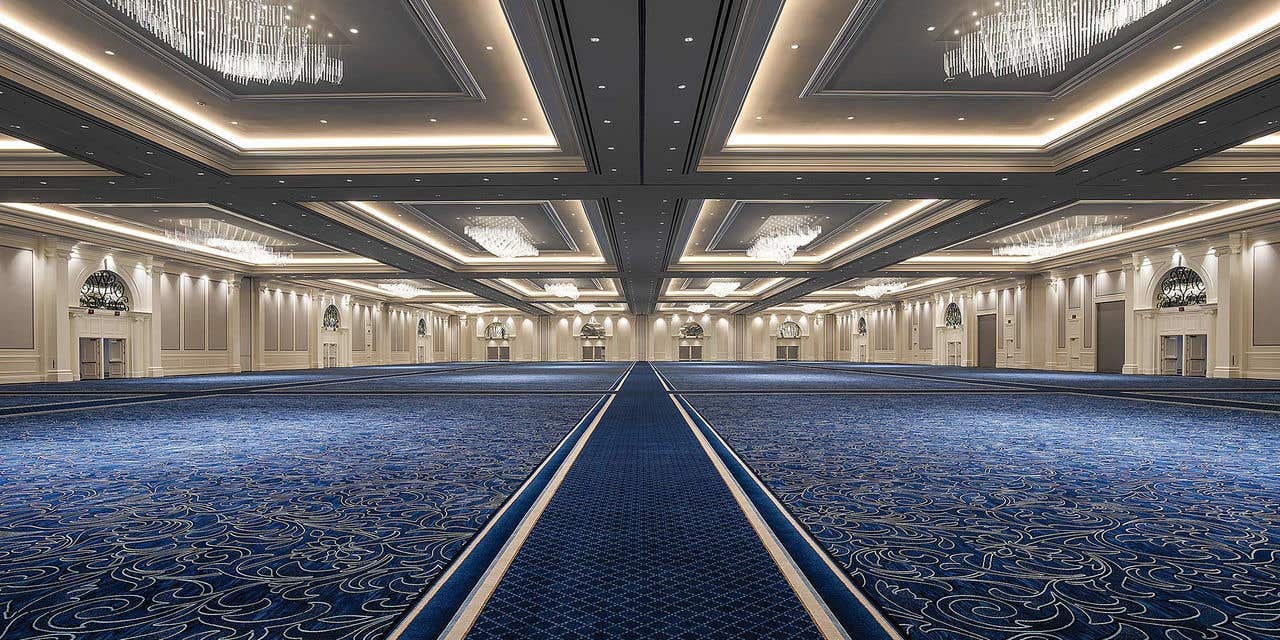 Large ballroom with blue carpet and chandelier above.