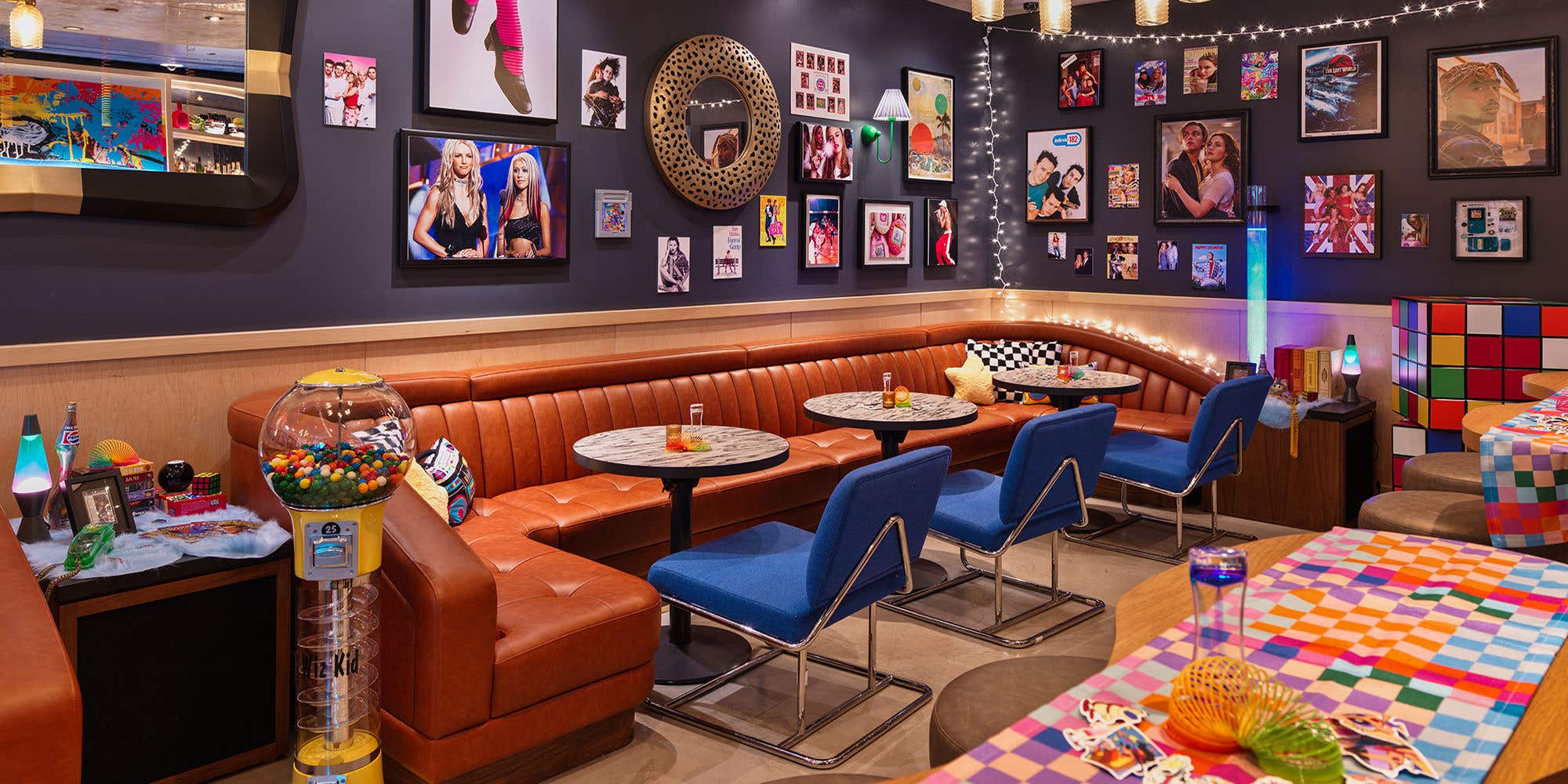 A bar with blue walls and chairs, and brightly colored art. String lights and 90s memorabilia are everywhere.