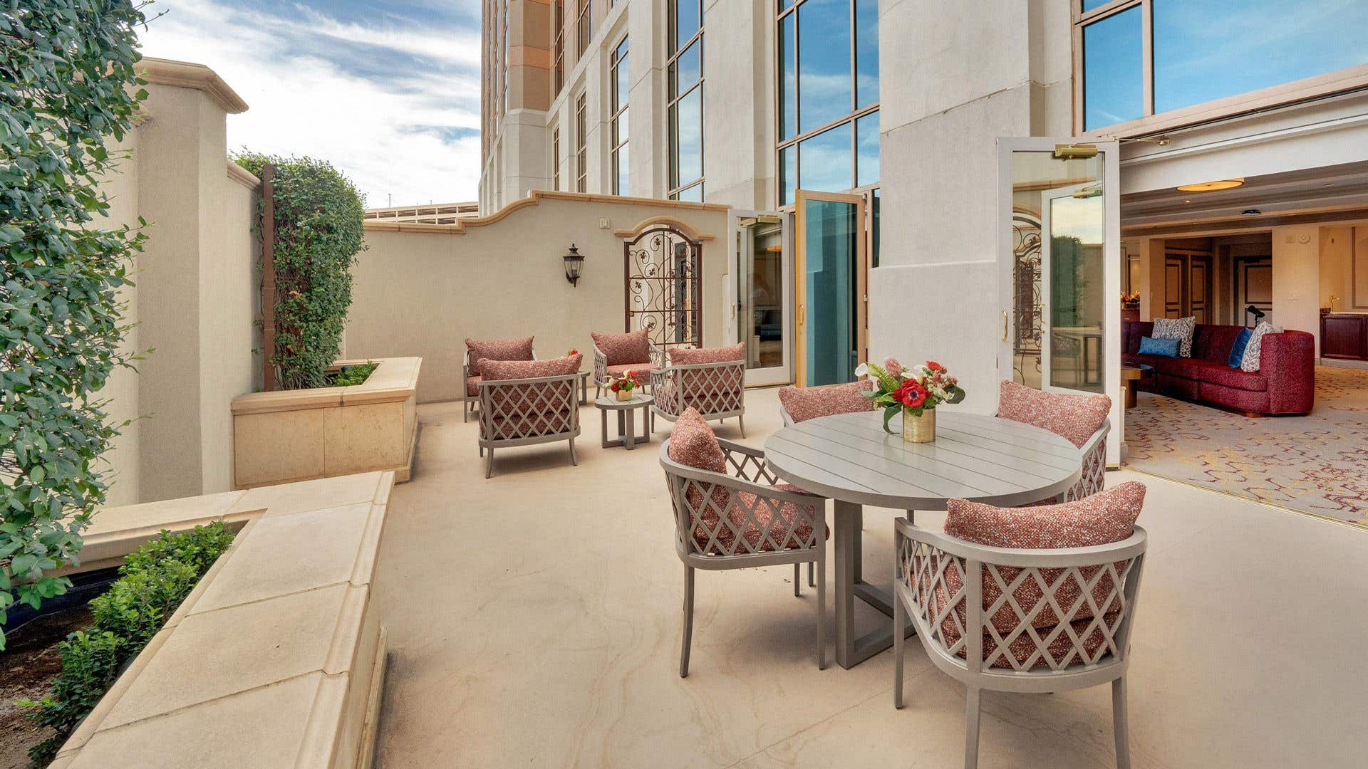 A spacious, private outdoor patio with stylish seating areas, lush greenery, and a view into the adjoining luxurious hotel suite.