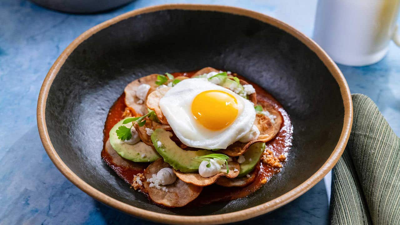 Bowl with a sunny-side egg over tortilla chips, avocado, and sauce.